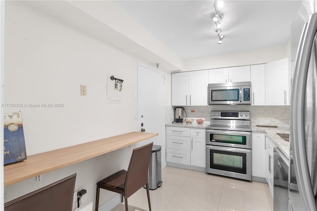 kitchen with tasteful backsplash, light stone counters, light tile patterned floors, white cabinets, and appliances with stainless steel finishes