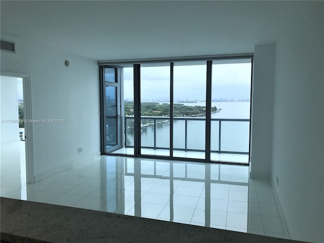 tiled spare room featuring a water view, a wall of windows, baseboards, and visible vents