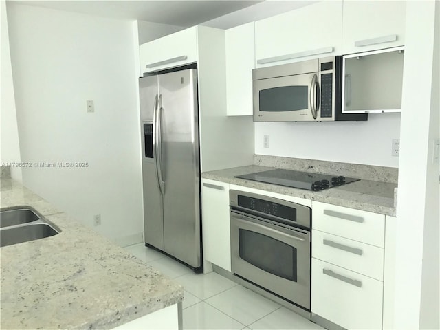 kitchen with white cabinetry, light stone counters, stainless steel appliances, and light tile patterned floors