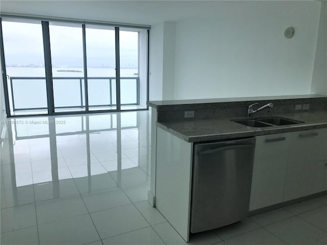 kitchen featuring dishwasher, light tile patterned floors, a sink, dark countertops, and white cabinets