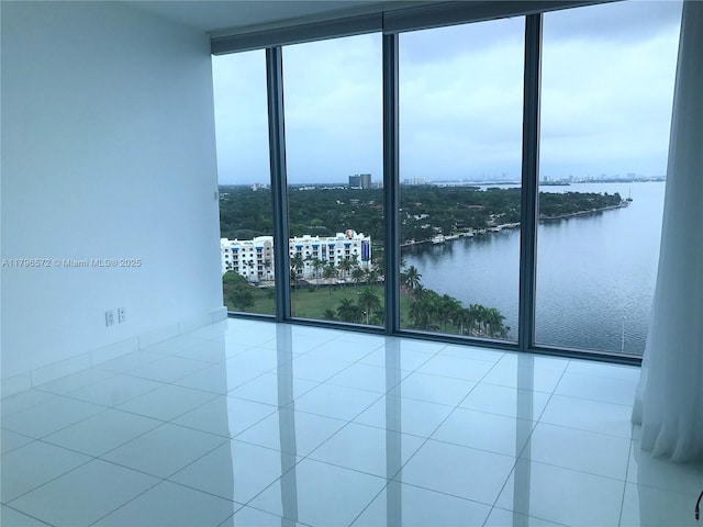 empty room featuring tile patterned floors, expansive windows, and a water view