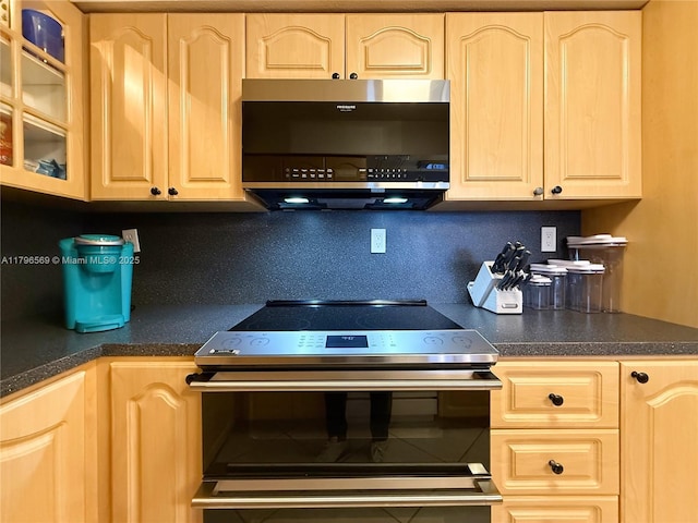 kitchen featuring dark countertops, light brown cabinetry, appliances with stainless steel finishes, and glass insert cabinets