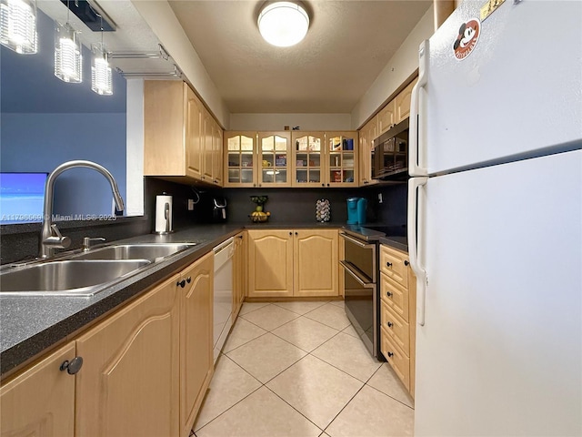 kitchen with light brown cabinetry, glass insert cabinets, a sink, dark countertops, and stainless steel appliances