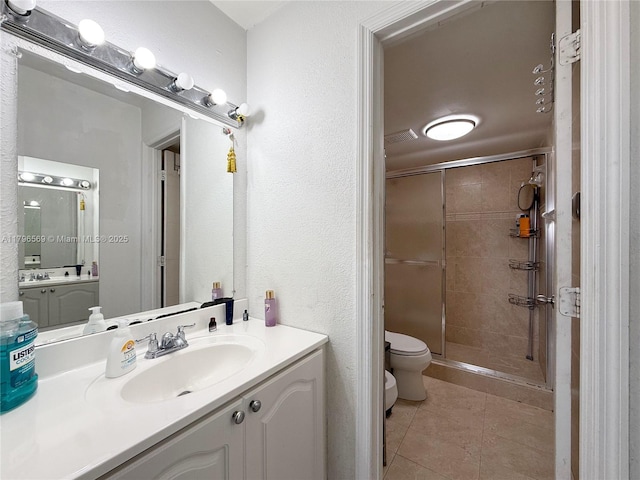 bathroom featuring toilet, tile patterned flooring, a shower stall, a textured wall, and vanity