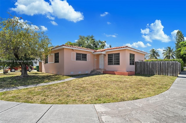 view of front of home featuring a tile roof, fence, stucco siding, and a front yard