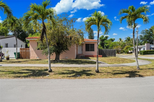 view of front of home featuring a front lawn, a tiled roof, stucco siding, and fence