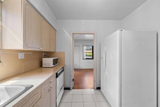 kitchen with a sink, white appliances, light tile patterned flooring, light countertops, and light brown cabinets