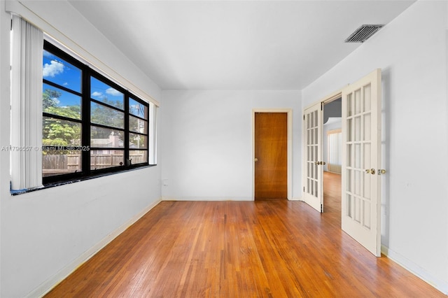 empty room featuring baseboards, visible vents, french doors, and wood-type flooring