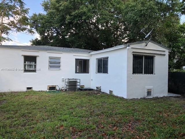 back of property with stucco siding, a lawn, and central AC