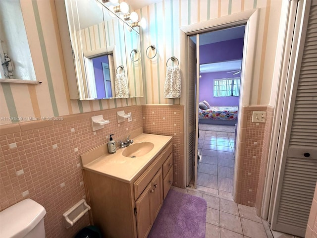 ensuite bathroom with tile walls, toilet, tile patterned flooring, vanity, and a wainscoted wall