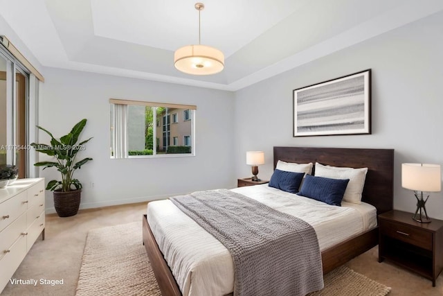 bedroom with a tray ceiling, light carpet, and baseboards