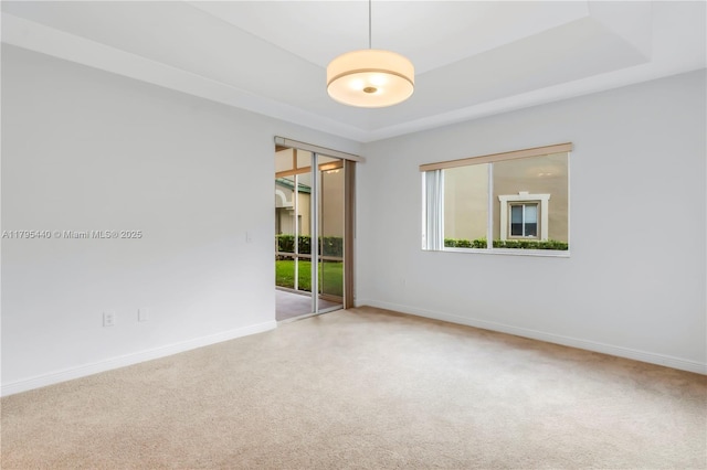 carpeted empty room with a raised ceiling and baseboards