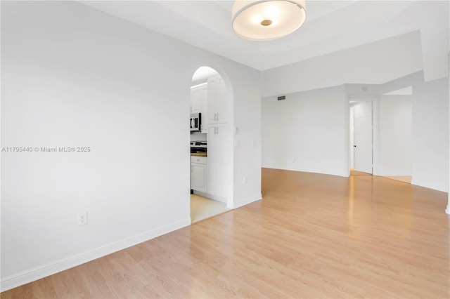 unfurnished room with baseboards, arched walkways, light wood-type flooring, and visible vents