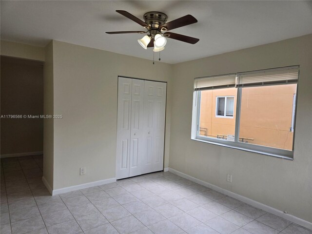 unfurnished bedroom featuring baseboards, tile patterned floors, a closet, and a ceiling fan