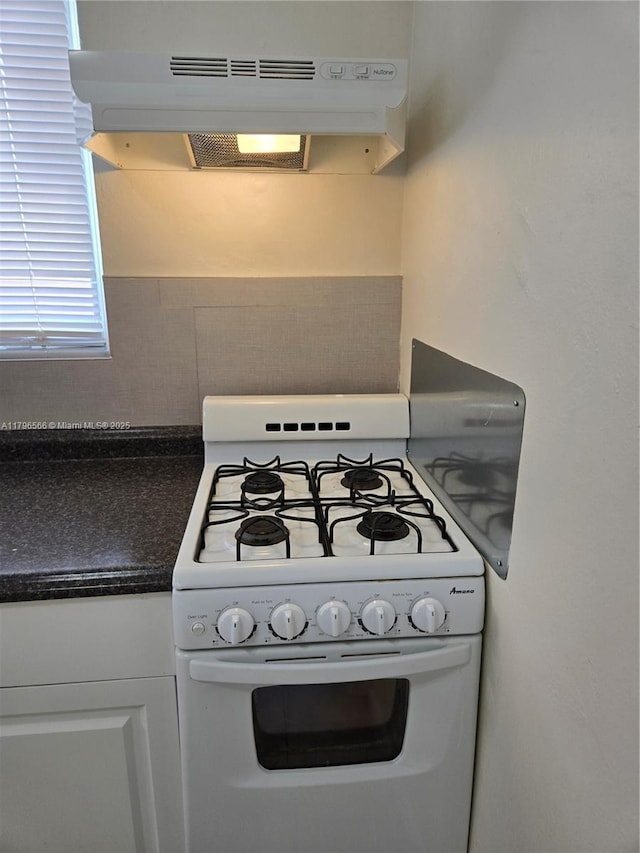 kitchen with gas range gas stove, backsplash, range hood, white cabinets, and dark countertops