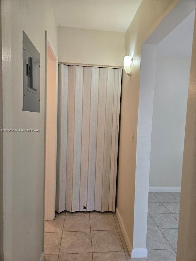 hall with light tile patterned floors, baseboards, and electric panel