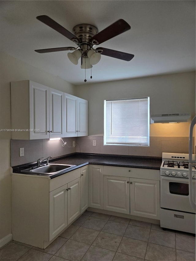 kitchen with dark countertops, under cabinet range hood, white cabinets, and white gas stove