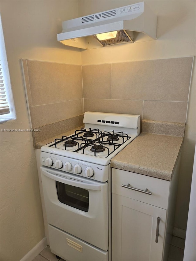 kitchen with white gas range oven, white cabinetry, backsplash, under cabinet range hood, and light countertops