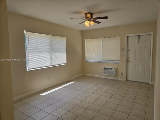 spare room with a wall mounted air conditioner, light tile patterned floors, baseboards, and a ceiling fan