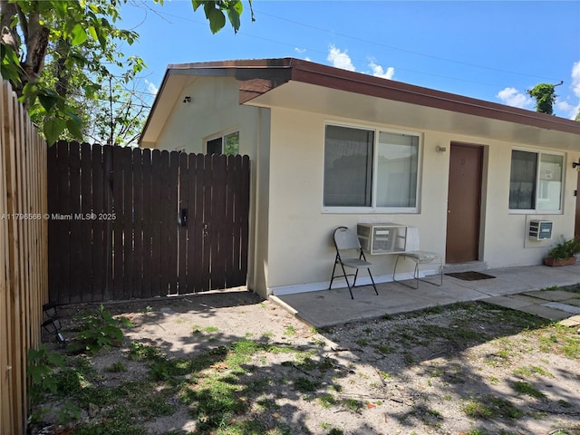 exterior space with stucco siding, an AC wall unit, fence, and a patio