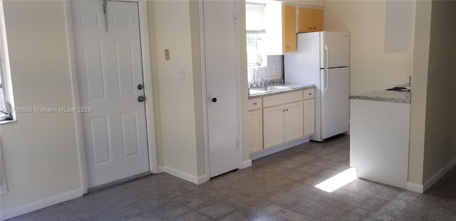 kitchen with freestanding refrigerator, baseboards, a sink, backsplash, and light countertops