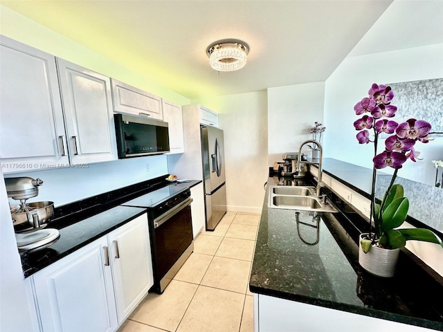 kitchen with light tile patterned floors, a sink, stainless steel fridge, white cabinets, and range with electric stovetop
