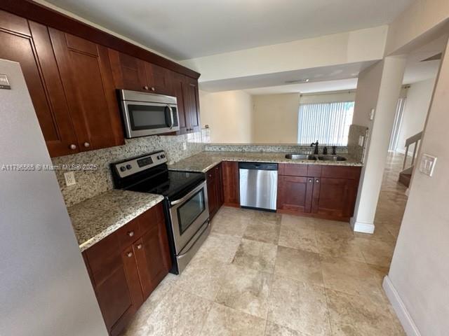 kitchen with appliances with stainless steel finishes, light stone counters, tasteful backsplash, and a sink