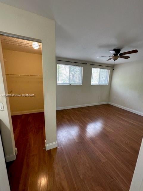 unfurnished bedroom featuring a ceiling fan, wood finished floors, baseboards, and multiple closets