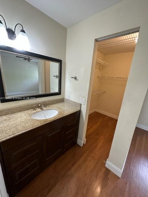 bathroom featuring baseboards, wood finished floors, vanity, and a spacious closet