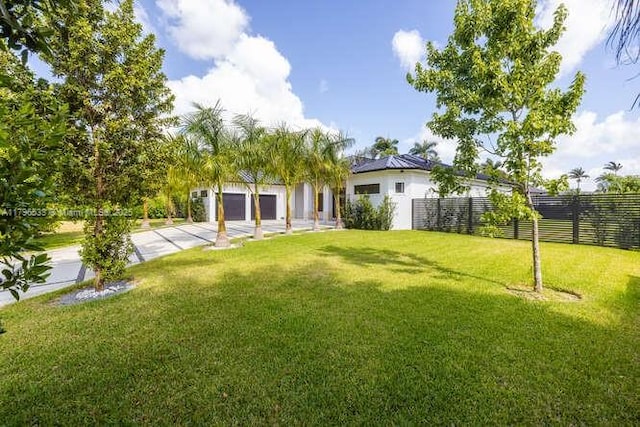 view of yard featuring concrete driveway, a garage, and fence