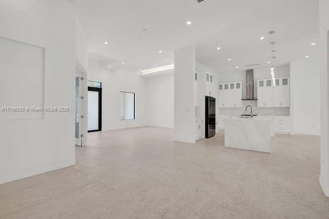 kitchen featuring a sink, open floor plan, white cabinets, a center island with sink, and wall chimney range hood