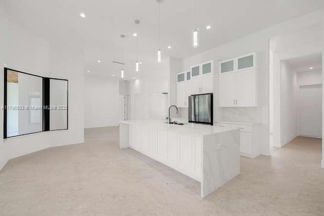 kitchen with freestanding refrigerator, glass insert cabinets, a sink, white cabinets, and a large island with sink