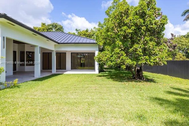 rear view of property with fence, a patio area, a yard, metal roof, and a standing seam roof