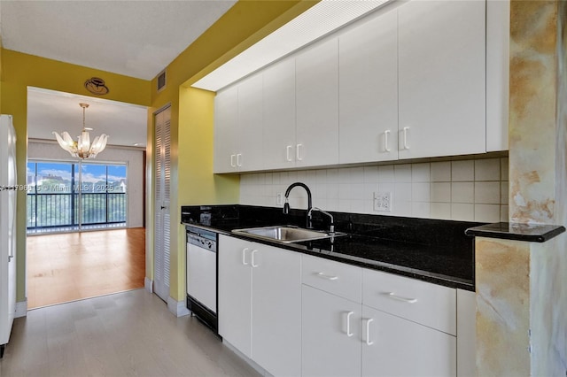 kitchen with light wood finished floors, a sink, a notable chandelier, backsplash, and dishwasher