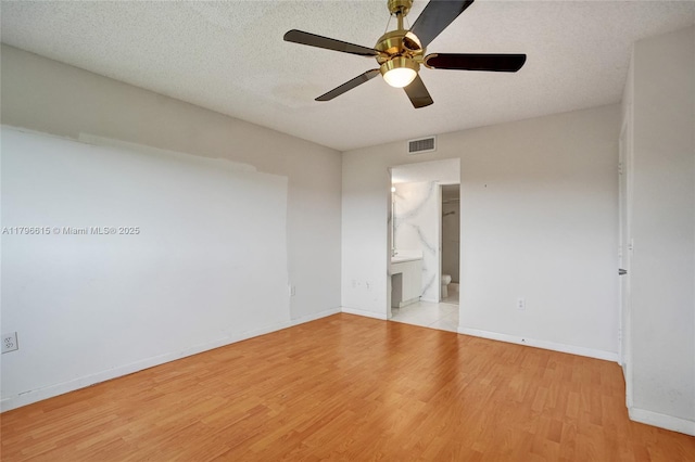 empty room featuring a textured ceiling, light wood-type flooring, visible vents, a ceiling fan, and baseboards
