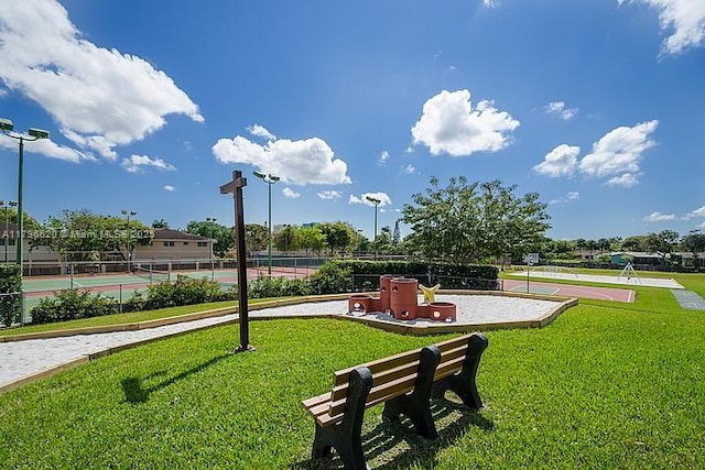 view of home's community featuring a yard, a tennis court, and fence