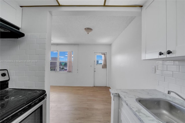 kitchen featuring light wood-style flooring, a sink, backsplash, white cabinets, and electric range