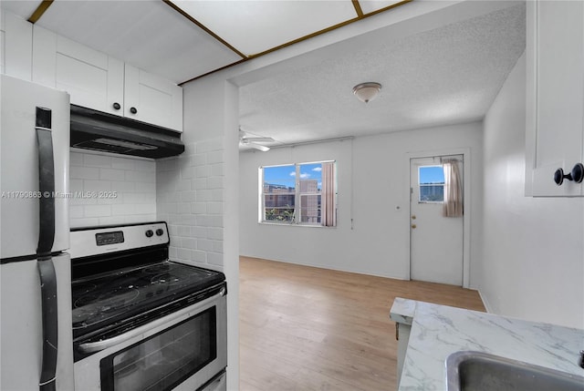kitchen with freestanding refrigerator, a wealth of natural light, stainless steel range with electric stovetop, and under cabinet range hood