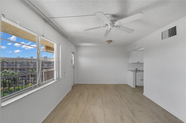 interior space with a healthy amount of sunlight, a textured ceiling, visible vents, and light wood-style floors