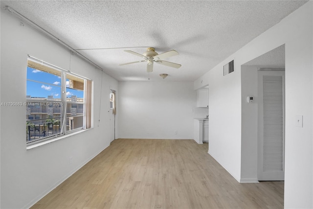 empty room featuring a textured ceiling, a ceiling fan, visible vents, and light wood-style flooring