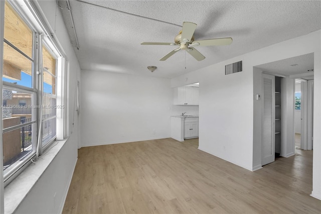 unfurnished living room with a textured ceiling, light wood-style floors, visible vents, and plenty of natural light