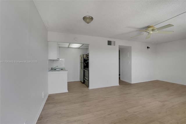 unfurnished living room with light wood-style flooring, a ceiling fan, a sink, a textured ceiling, and visible vents