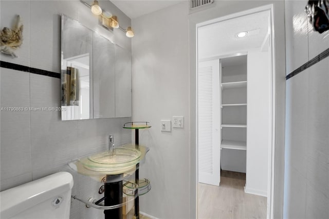 bathroom with toilet, wood finished floors, a sink, visible vents, and baseboards
