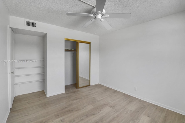 unfurnished bedroom with a closet, a textured ceiling, baseboards, visible vents, and wood finished floors