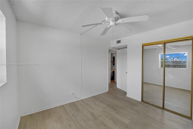 unfurnished bedroom featuring wood finished floors, a closet, a textured ceiling, visible vents, and ceiling fan