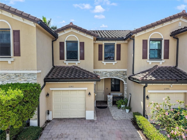 mediterranean / spanish house with an attached garage, a tiled roof, and stucco siding
