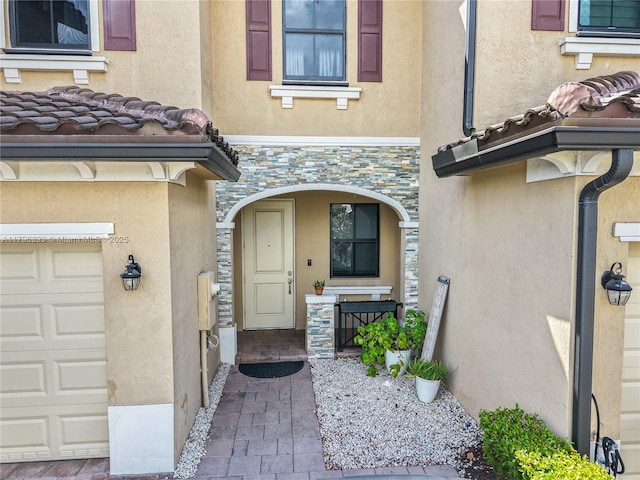 view of exterior entry with stone siding, stucco siding, covered porch, and a garage