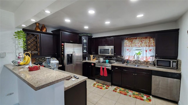 kitchen with a sink, a peninsula, stainless steel appliances, backsplash, and light tile patterned floors