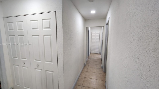 corridor featuring a textured wall, baseboards, and light tile patterned floors