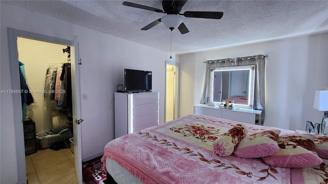 bedroom featuring a textured ceiling, a spacious closet, a ceiling fan, and tile patterned floors